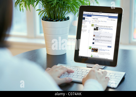 Jeune femme la lecture et la mise à jour de la page Facebook sur un iPad connecté via la technologie sans fil Bluetooth Banque D'Images