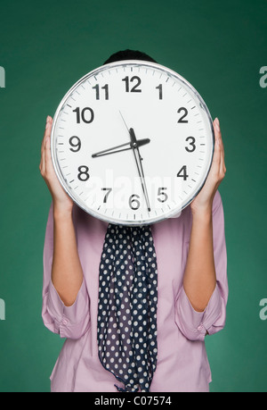 Businesswoman holding une horloge en face de son visage Banque D'Images