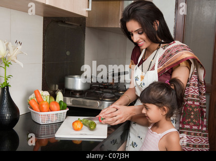 Femme hacher les légumes dans la cuisine avec sa fille Banque D'Images