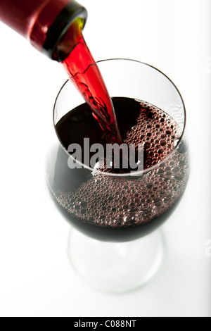Un verre de vin rouge est versé à partir de la bouteille sur un fond blanc. Banque D'Images