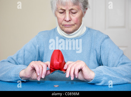 Les personnes âgées pauvres femme pensionné qui n'a pas d'argent et une expression inquiète vidange d'un penny coin arrière sur une bourse dans l'âge de l'austérité. England UK Banque D'Images