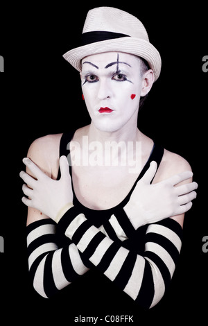 Studio portrait de clown théâtral sérieux en blanc à rayures avec gants et chapeau coeurs rouges sur son visage isolé sur zone noire Banque D'Images