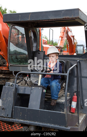 Bébé garçon portent un casque est assis dans le siège du conducteur d'une machine à vapeur sur un site de construction à Anchorage Banque D'Images