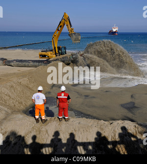 Les spectateurs à regarder alors qu'un remorqueur est sable de pompage par l'intermédiaire d'un flexible sur une plage pour les plages ou la régénération des plages Banque D'Images