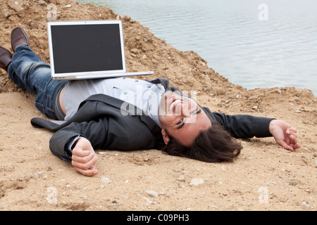 Jeune homme avec un ordinateur portable posé sur une plage du lac Laughing Banque D'Images