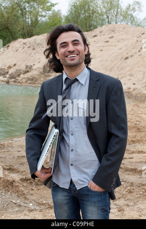 Jeune homme souriant avec ordinateur portable sur une plage du lac Banque D'Images