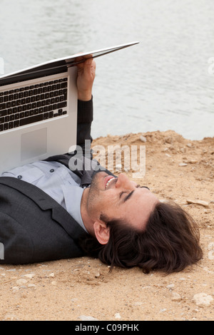 Jeune homme avec un ordinateur portable posé sur une plage du lac de penser Banque D'Images