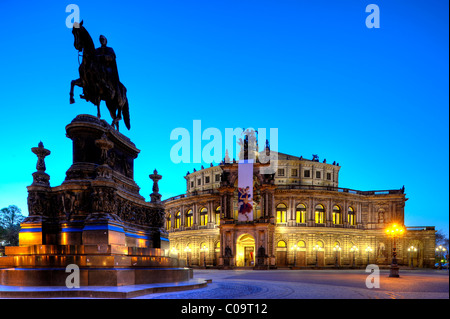 Scène de nuit, illuminé de l'opéra Semperoper avec drapeaux et Koenig-Johann-Denkmal monument sur la place Theaterplatz Banque D'Images