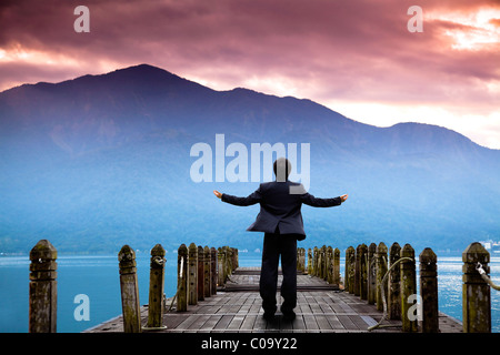Businessman debout sur la jetée et regarder la montagne et nuages de l'aube Banque D'Images