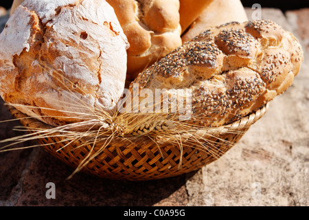 Un gros plan d'un panier à pain avec une variété de pains et de blé sur table en pierre. Banque D'Images