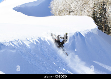 Motoneige sur montagne en hiver sautant par dessus une corniche dangereuse sur haute colline raide sur de grandes corniches dangereuses. Banque D'Images