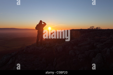 Hill Walker en regardant vers le soleil de Setting sur les cicatrices de Twisleton balance Moor Yorkshire Dales Royaume-Uni Banque D'Images