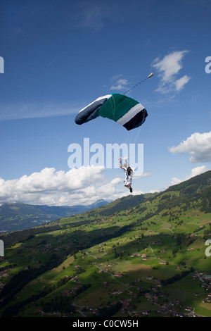 Parachutiste sous voile est en vol entre les nuages et le long des montagnes de plus de champs verts. Banque D'Images