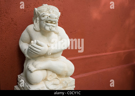 Balinais blanc sculpté en pierre sculpture démon sur un mur rouge en terre cuite, Ubud, Bali, Indonésie. Banque D'Images