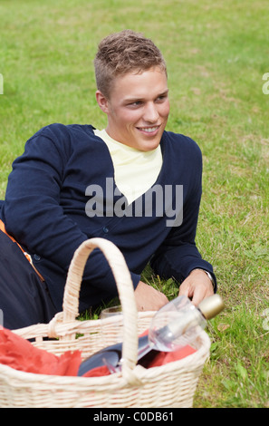 Jeune garçon blond allongé sur l'herbe avec panier pique-nique Banque D'Images