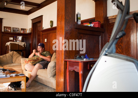 La Grange, California, United States. Jeune mange son petit-déjeuner sur le canapé en regardant la télévision. Banque D'Images