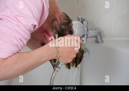 Woman bending over bath shampooing rincer les cheveux lavés hors tenant une tête de douche à main droite Banque D'Images