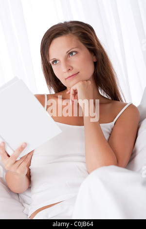 Femme penser lors de la lecture du livre blanc sur canapé Banque D'Images