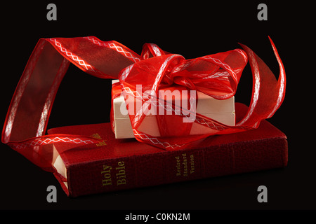 Avec Bible rouge blanc chèques cadeaux enveloppés de ruban rouge sur fond noir, simple représente un événement précieux. Banque D'Images