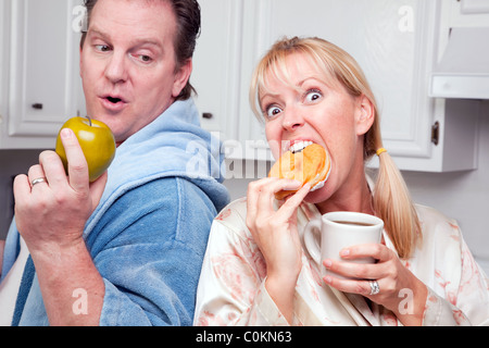 Couple humoristique dans la cuisine manger beigne et Café ou fruits sains. Banque D'Images
