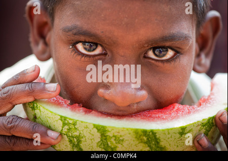 Heureux les jeunes Indiens de caste inférieure pauvre garçon des rues de manger une tranche de pastèque. Close up portrait Banque D'Images