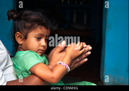 Indian girl sitting on granddads genoux en appui sur la prière les mains. L'Andhra Pradesh, Inde Banque D'Images