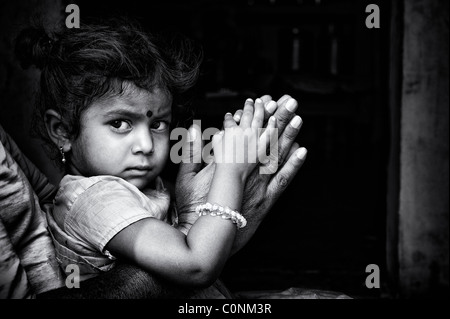 Indian girl sitting on granddads genoux en appui sur la prière les mains. L'Andhra Pradesh, Inde. Noir et blanc. Banque D'Images