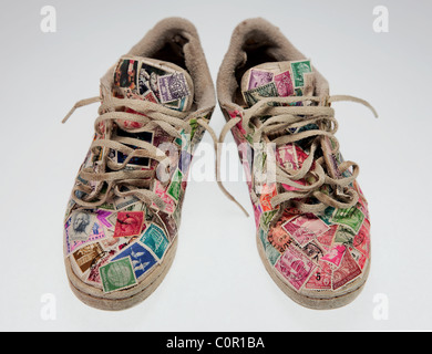 Une paire de chaussures de course usés recouverts de vieux timbres-poste sur un fond clair Banque D'Images