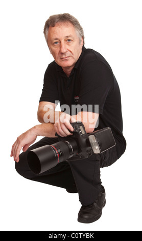 Mâle adulte, vêtu de noir accroupi tenant un appareil photo reflex numérique professionnel, isolé sur un fond blanc. Banque D'Images