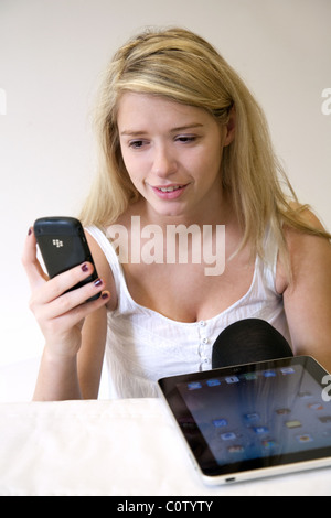 Blonde teenage girl holding téléphone mobile Blackberry avec l'iPad en face d'elle en souriant Banque D'Images