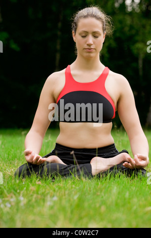 Young adult woman practicing yoga on un champ entouré d'arbres Banque D'Images