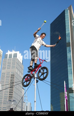 Artiste de rue l'équilibre entre son vélo BMX sur une corde raide tout en jonglant avec des torches de feu, la ville de Sydney, NSW, Australie. Banque D'Images