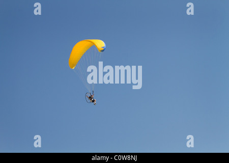 L'homme vole dans un ciel bleu sur un parglider avec un auvent jaune. Banque D'Images