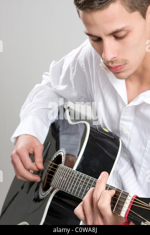 Un jeune homme en chemise blanche strum une guitare acoustique. Banque D'Images