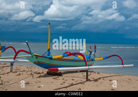 Bateau de pêche balinaise colorée appelée jukung en plein soleil contre un ciel de mousson sur la plage de Sanur, Bali Indonésie Banque D'Images