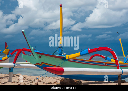 Bateau de pêche balinaise colorée appelée jukung en plein soleil contre un ciel de mousson sur la plage de Sanur, Bali Indonésie Banque D'Images