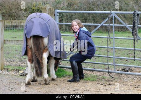 Jeune cavalière avec son poney qui a repéré certains frais herbe à manger à l'extérieur d'un champ Banque D'Images