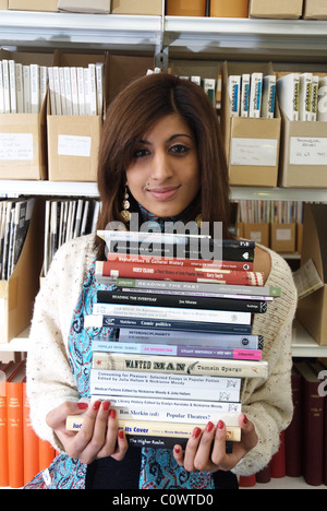 Jeune femme dans une bibliothèque universitaire portant une pile de livres Banque D'Images