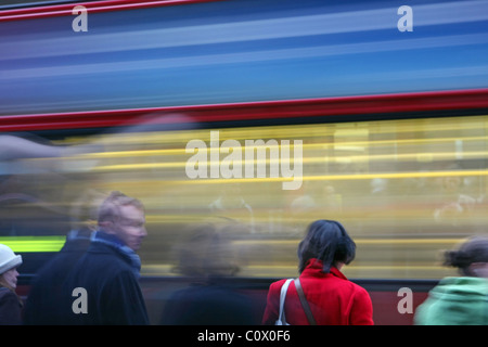 Les gens qui attendent de traverser la route avec une impression floue d'un bus passant red London Banque D'Images