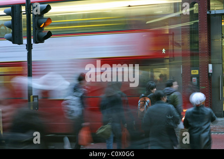 Les personnes qui traversent la route aux feux de circulation avec une impression floue d'un London bus rouge passant de l'autre côté de la route Banque D'Images