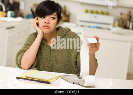 Jeune femme multi-ethnique tourmenter au sujet des calculs financiers dans sa cuisine. Banque D'Images