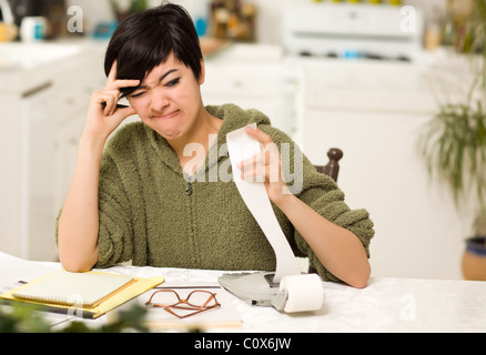 Jeune femme multi-ethnique tourmenter au sujet des calculs financiers dans sa cuisine. Banque D'Images