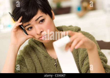 Jeune femme multi-ethnique tourmenter au sujet des calculs financiers dans sa cuisine. Banque D'Images