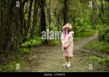 Fille en imperméable rose un jour de pluie à pied dans les bois, Nouvelle-Zélande Banque D'Images