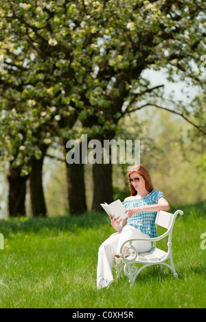 Red hair woman reading book sur banc blanc dans un pré ; shallow DOF Banque D'Images