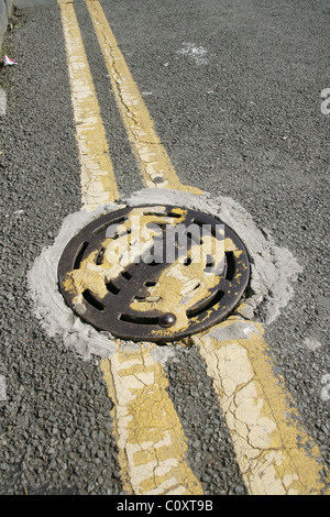 Manhole et double lignes jaunes sur la route de rue au Pays de Galles grande-bretagne uk Banque D'Images