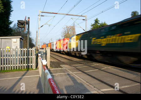 Le train de marchandises longue traverse un passage à niveau sans pilote dans l'Essex, au Royaume-Uni. Les barrières ne sont pas d'arrêt rouge et clignote. Banque D'Images