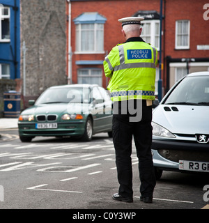 Vue arrière d'un agent de la circulation à regarder les voitures qui circulent sur une rue de ville, pays de Galles, Royaume-Uni Banque D'Images