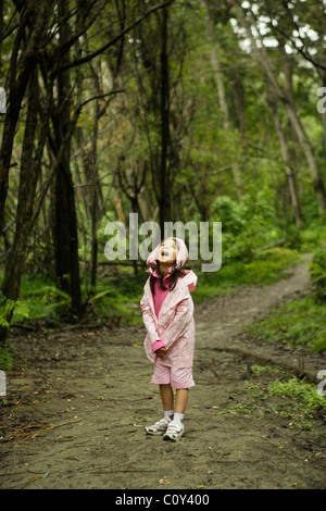 Fille en imperméable rose un jour de pluie à pied dans les bois, Nouvelle-Zélande Banque D'Images