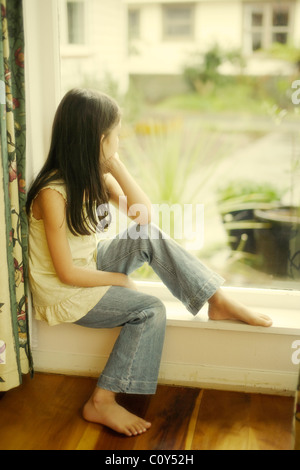 Fille est assise par fenêtre sur jour de pluie Banque D'Images